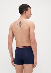 Un caleçon bleu marine ajusté avec une ceinture rayée contrastante. Le tissu semble lisse avec un léger élasticité.