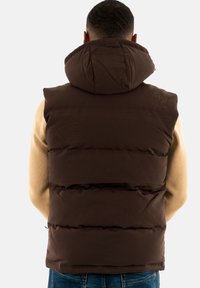 Brown puffy vest with a hood, featuring horizontal quilted sections. Material appears smooth and insulated. Subtle branding on the upper back.