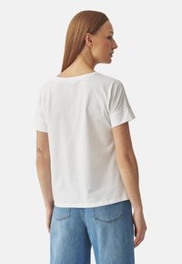 T-shirt blanc à manches courtes avec une coupe décontractée, fabriqué en coton doux, dotée d'un col rond et de détails de couture subtils.