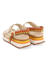 Sandalias beige con tiras trenzadas en naranja, amarillo y marrón. Plataforma gruesa blanca con rayas amarillas y naranjas y suela de goma.