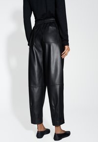 Schwarze Leder-Hosen mit weitem Bein und elastischem Bund, ausgestattet mit zwei Gesäßtaschen, einer glatten Textur und einer verkürzten Länge.