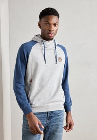 Sudadera gris con mangas azules, cuello con cordones y un parche de cuero con el logo. Presenta un bolsillo tipo canguro y puños acanalados.