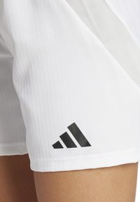 Witte sportieve shorts van textuurstof met een mesh-paneel. Zwart Adidas-logo op de linkerbenedenhoek. Eenvoudig, functioneel ontwerp.