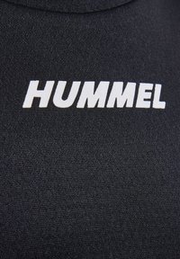 Svart tyg med en texturerad yta som har ordet "HUMMEL" i fet stil vita bokstäver. Designen är enkel och fokuserad på varumärket.