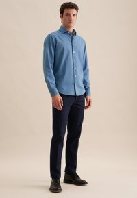 Lichtblauw overhemddasje van katoen, gecombineerd met marineblauwe broek. Het overhemd heeft een kraag en lange mouwen, met een gladde textuur.