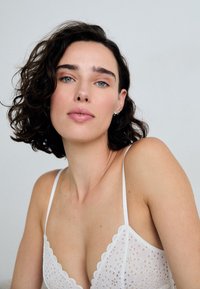 White lace bralette with scalloped edges, featuring a floral pattern and thin straps. Smooth texture and minimal hardware details.