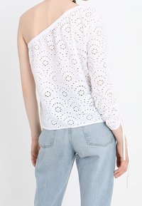 Hvid off-shoulder top med hulmønster, tekstureret stof, en langærmet og snøre detaljer. Kombinationen med lyseblå jeans.