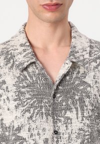 Camicia a maniche corte in tessuto testurizzato bianco e nero con un motivo floreale, dotata di colletto e bottoni neri.