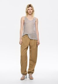 Canottiera in maglia argentata, pantaloni beige a gamba larga e sandali con tacco metallici. La canottiera ha una vestibilità comoda e bordi a coste.