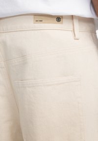 Beige pamut nadrág, texturált felülettel, "EST. 1992" felirattal ellátott címkével és hátsó zsebbel a tárolás érdekében.