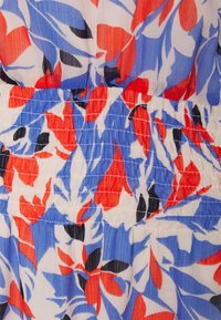 Acercamiento de una tela con un patrón floral abstracto en rojo, azul, negro y blanco, con detalles de costura elástica horizontal fruncida.