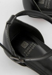 Sandalias de tacón negro con un elegante upper de cuero, diseño de punta abierta, tira en el tobillo y plantilla acolchada con el logo "FOREVER COMFORT".