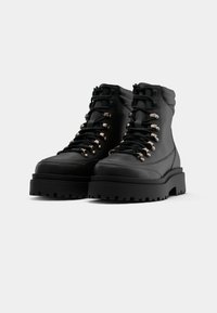 Fekete bőr bokacsizmák vastag, texturált talppal, fémes cipőfűzőkkel, valamint párnázott gallérral a kényelmes viselet érdekében.