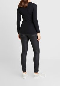 Svart långärmad topp med figurnära design, matchad med svarta stretchbyxor. Modellen bär vita sneakers. Slät tygkvalitet och grundläggande stil.