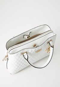Borsa a tracolla bianca imbottita con hardware dorato, doppi manici superiori, chiusura a zip e un design elegante. Presenta tasche interne e dettagli con logo.