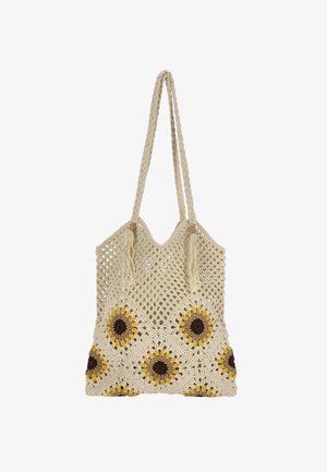 Hahtuvasta virkattu kassi kermaan vivahtavassa värissä, jossa on keltaisia ja ruskeita auringonkukkakuvioita. Kassissa on punotut kahvat ja tupsut, ja se esittelee avointa kudontaa.