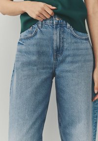 Lichtblauwe high-waisted jeans van denim. Kenmerken zijn onder andere een sluiting met een knoop aan de voorkant, vijf zakken en gestikte details langs de naden.