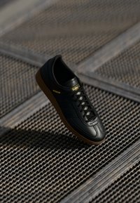 Scarpa sportiva in pelle nera con suola in gomma, con tre strisce nere, parte superiore testurizzata e marchio dorato etichettato 'Spezial'.