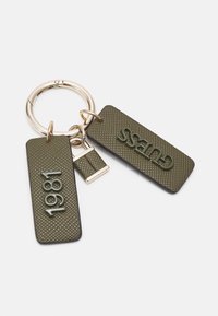 Nyckelring med texturerade olivgröna taggar, en som visar "1981" och den andra "GUESS" i upphöjda bokstäver, fästa vid en guldring.
