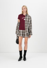 Marlboro t-shirt with white star graphic, layered with a plaid oversized shirt, paired with a plaid skort, black knee-high socks, and heels.