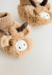 Chaussons en peluche de couleur beige avec une forme arrondie, des poignets en tricot marron et un visage d'animal décoratif avec des cornes et des détails de nez dans des textures contrastées.