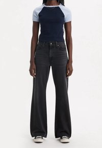 Mustat väljähaalarit korkea vyötärö, yhdistettyinä tummansiniseen ja vaaleansiniseen raglanhihaiseen t-paitaan. Puuvillamateriaali, joka on sileästä tekstuurista.