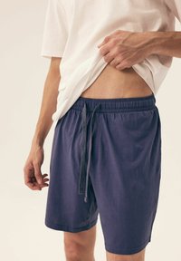 Granatowe, lekkie szorty stretchowe z elastycznym paskiem i sznurkiem. Gładka tekstura, długość do kolan, stylizowane z białym t-shirtem.