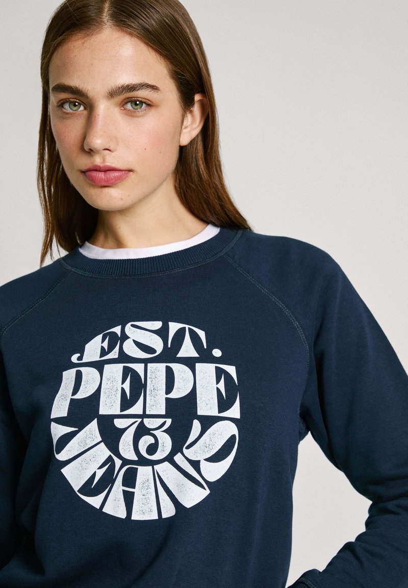 Sweatshirt marine à manches raglan, avec un grand design graphique en texte blanc qui indique "EST. PEPE JEANS." Texture douce, coupe décontractée.