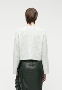 Ανοιχτό γκρι, κομμένο πλεκτό πουλόβερ με υφαμένη υφή, φαρδιές μανίκες και στρογγυλή λαιμόκοψη, συνδυασμένο με μακριά μαύρη δερμάτινη φούστα με φρουφρού.