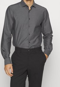 Chemise gris foncé à manches longues avec un petit motif à points, dotée d'un col boutonné et de boutons noirs ; associée à un pantalon noir.