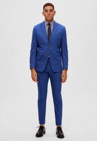 Royal blue suit with two buttons, notch lapels, and flap pockets. Paired with a striped shirt, tie, and polished black shoes. Tailored fit.