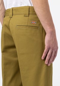 Olivgröna byxor med en avslappnad passform, med bakfickor och en Dickies-logopatch. Tillverkade av slitstarkt tyg med en slät struktur.