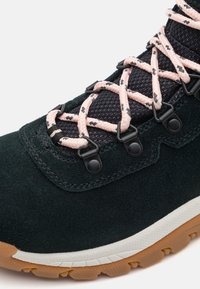 Tmavě zelená suede turistická bota s černou síťovinou a růžovými tkaničkami. Obsahuje plastové háčky, bílou mezipodešev a gumovou podrážku s texturovaným designem.