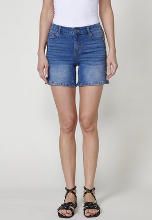 Shorts en denim de couleur bleu décoloré, au design ajusté, avec des poches latérales. Présente un accent en chaîne décoratif le long du côté droit.