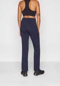 Marinblå, figurnära träningsbyxor i stretchigt tyg med slät yta och en elastisk midjeresår, kombinerade med svarta sneakers.