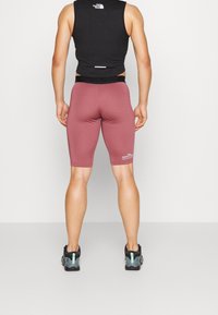Czarny bezrękawnik, dopasowane bordowe szorty i czarne buty sportowe z miętowymi akcentami. Na końcu szortów znajduje się logo "The North Face".