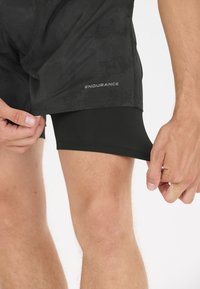 Svarta sportshorts med ett innerlager, med en slät yta och ett subtilt mönster. Ordet "ENDURANCE" är tryckt på ytterlagret.