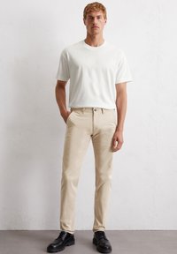 Witte katoenen t-shirt met ronde hals voor heren, gecombineerd met beige katoenen broek. Zwarte veterschoenen maken de outfit compleet. Eenvoudig ontwerp en neutrale kleuren.