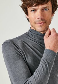 Maglietta grigia a collo alto a costine con un design aderente, maniche lunghe e una consistenza morbida. Stile minimalista con un collo pulito.