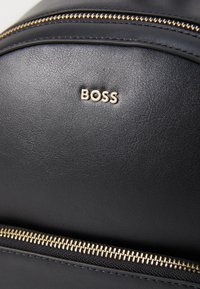 Zaino in pelle nera con superficie texturizzata, caratterizzato da una cerniera dorata e dal logo "BOSS" impressa in oro.