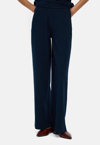 Granatowe spodnie o szerokich nogawkach z miękkiego materia�łu, z wysokim stanem i kieszeniami bocznymi, zestawione z brązowymi butami na szpilce.