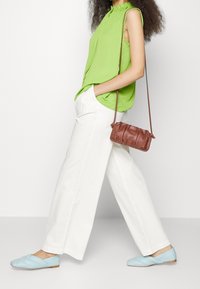 Grünes ärmelloses Top, weiße weite Hosen, bläuliche Schuhe mit geflochtenen Details und eine kleine braune Umhängetasche. Einfaches und modernes Outfit.