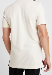 Jasny beżowy t-shirt wykonany z miękkiej bawełny, z krótkimi rękawami, luźnym krojem i bocznymi rozporkami z kontrastowymi akcentami na dole.