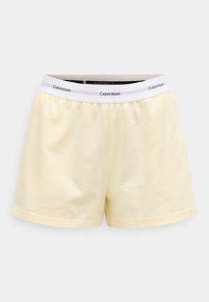 Lys gule bomullsshorts med hvit elastisk linning med gjentakende svart "Calvin Klein"-logo, vist på ensfarget hvit bakgrunn.