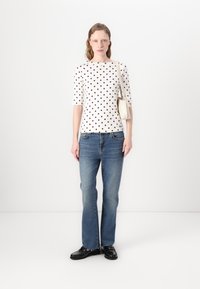 Haut blanc à pois avec des manches trois-quarts, associé à un jean en denim bleu clair et des chaussures noires, tenu avec un sac à bandoulière beige.