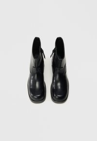 Botines de cuero negro hasta el tobillo, con punta redonda, textura lisa, cierre lateral con cremallera y diseño minimalista. Suela plana de goma.