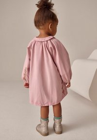 Vestito di cotone rosa con maniche lunghe e colletto rotondo, caratterizzato da ricami floreali lungo la manica. Paio di stivali argentati e calze verdi.