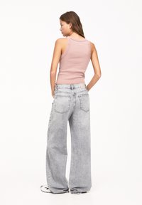 Top senza maniche di colore rosa chiaro a coste abbinato a jeans in denim grigio chiaro dal taglio morbido. I jeans presentano tasche posteriori e una texture sbiadita.
