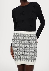 Haut noir à manches longues avec des motifs papillons texturés, associé à une mini-jupe ajustée à motifs noir et blanc, dotée d'une ceinture en tricot.