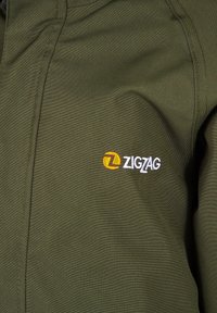 Olijfgroene jas met een gladde textuur, voorzien van een opvallend geel en wit geborduurd "ZIGZAG" logo op de borst.